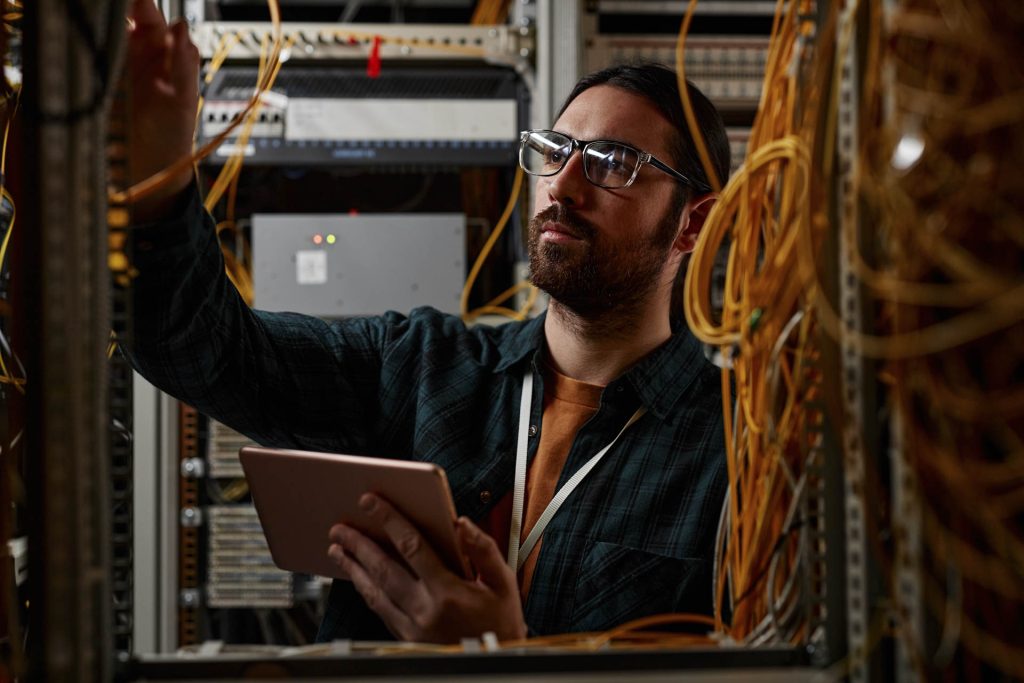 bearded man setting up server while working with data network holding tablet